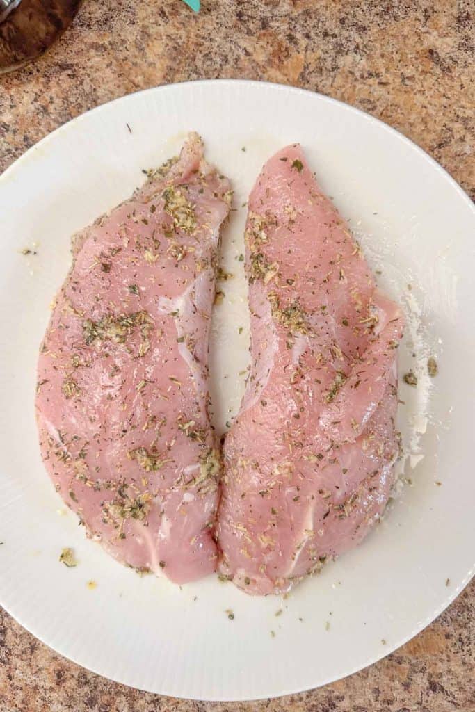 Two turkey tenderloins on a plate with herbs on them.