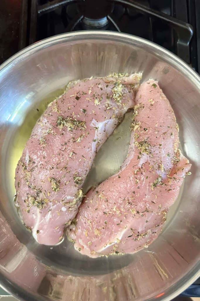 Two pieces of meat in a pan on a stove.