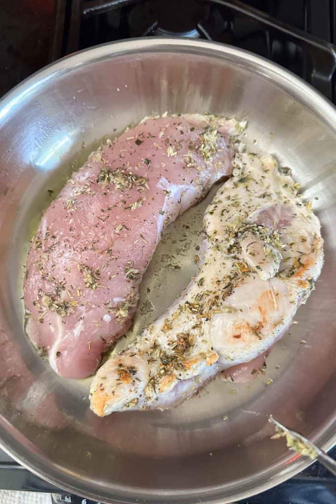 Turkey tenderloins in a pan with herbs on the stove.