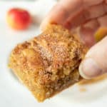 A person holding a small piece of cinnamon apple squares.