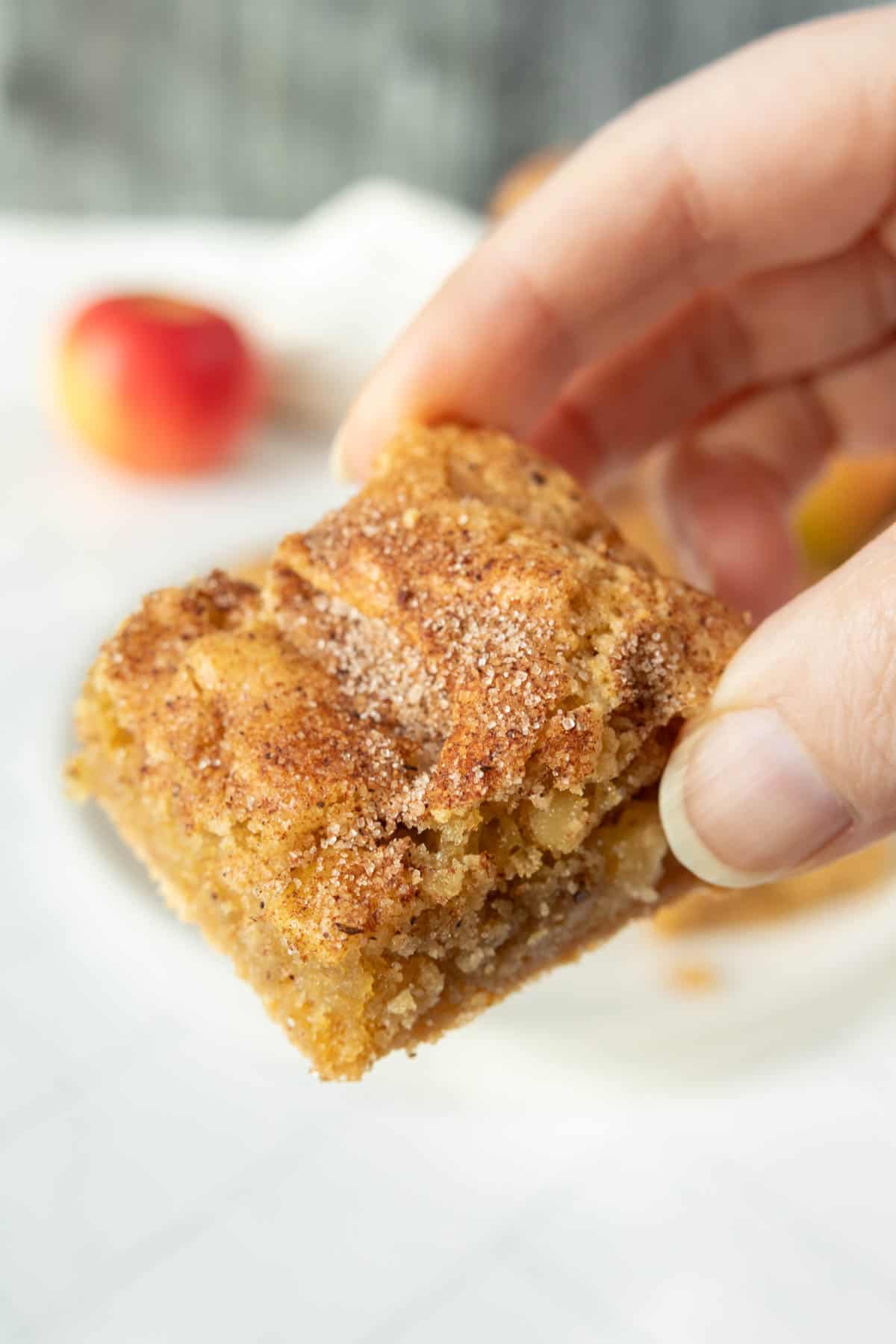 A person holding a small piece of cinnamon apple squares.