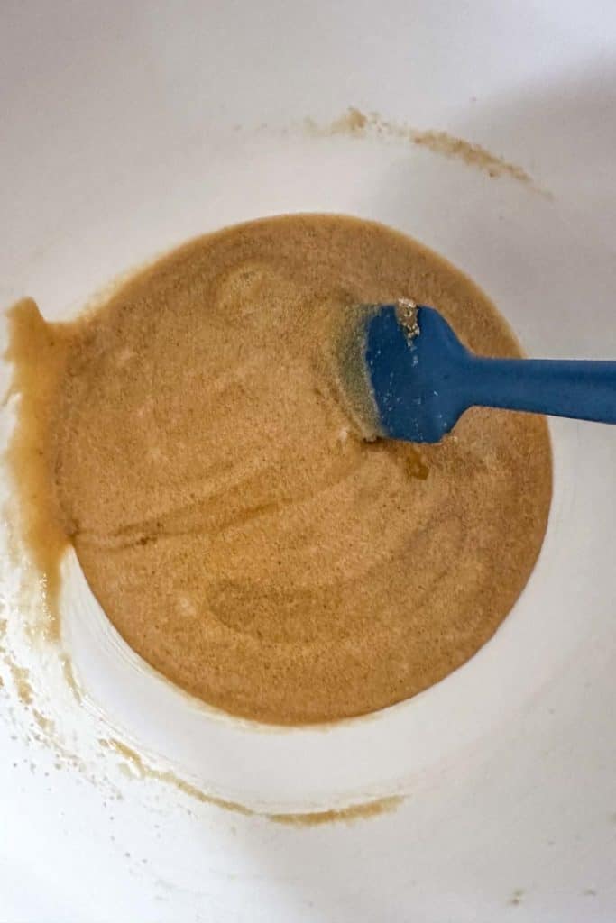 A blue spoon is being used to stir a brown mixture in a bowl.
