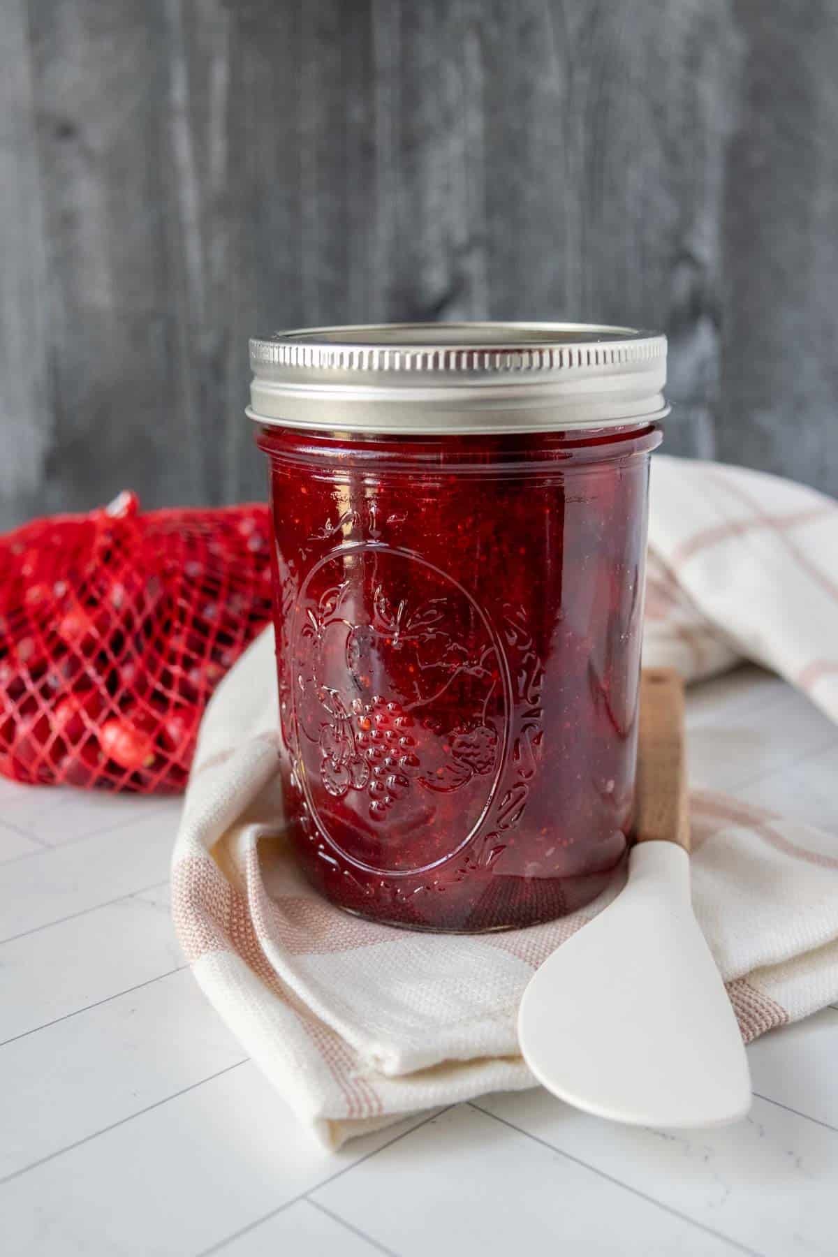 A jar of cranberry jam with a spoon next to it.
