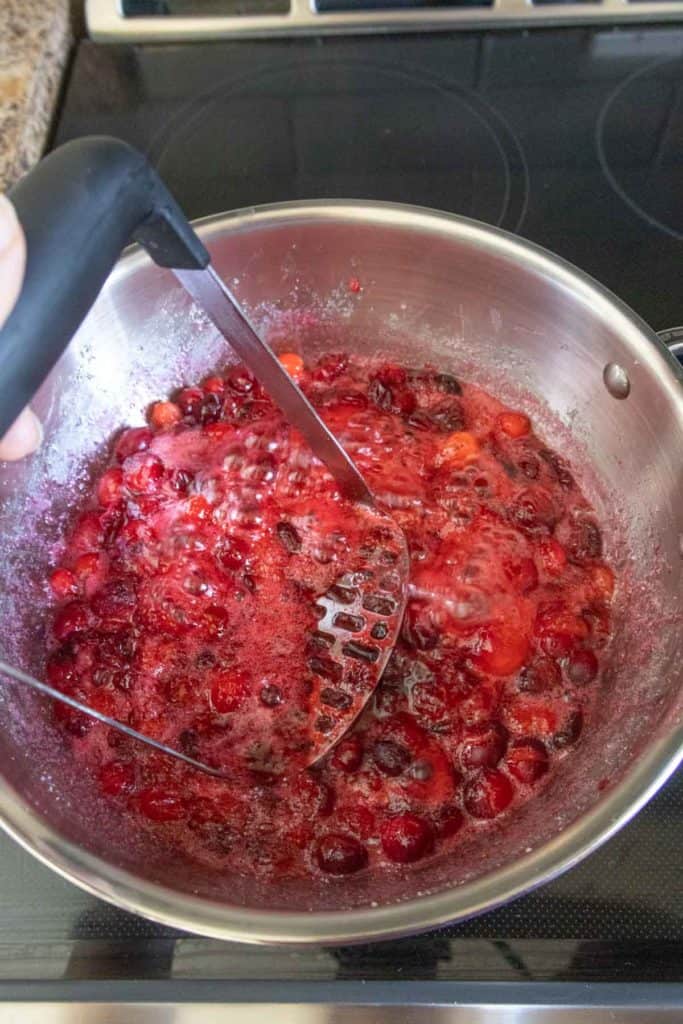A person stirring cranberries in a pan on the stove.