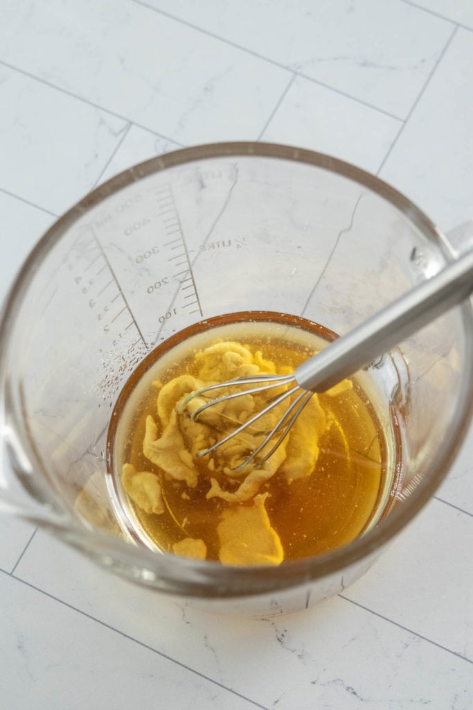 A glass bowl filled with liquid and a whisk.