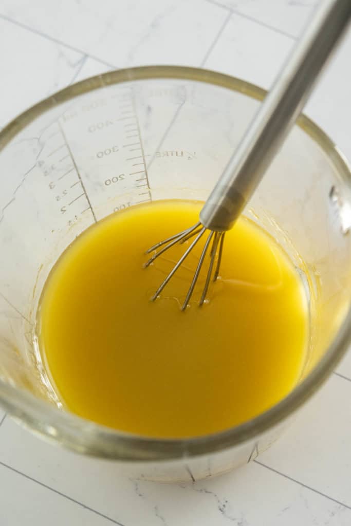 A glass bowl filled with a yellow liquid and a whisk.