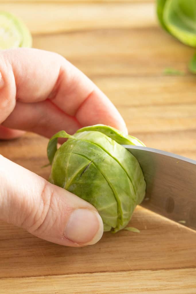 A person cutting brussels sprouts with a knife.