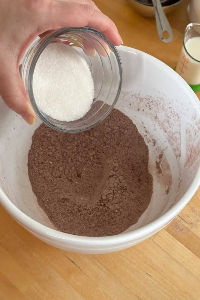 A person pouring sugar into a bowl of chocolate.