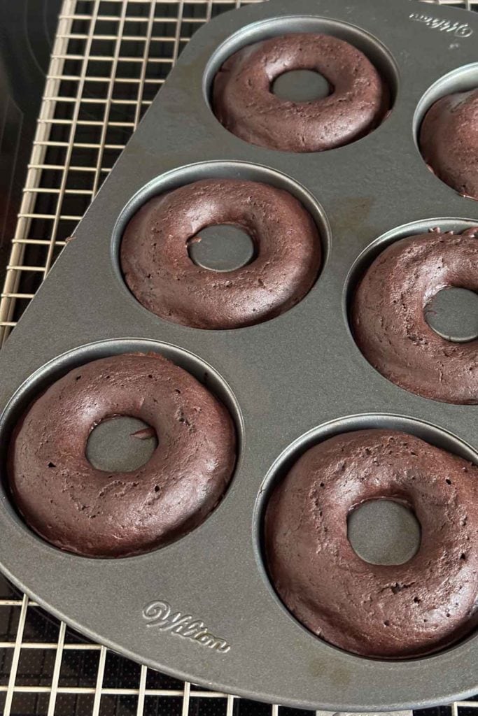 Chocolate donuts in a pan on a cooling rack.
