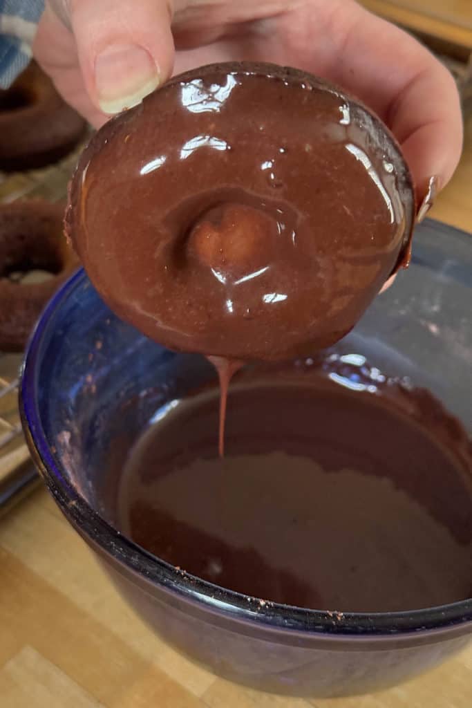 A person pouring chocolate over a doughnut in a bowl.