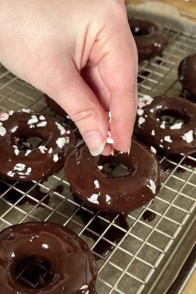 A person dipping a donut in chocolate and sprinkles.