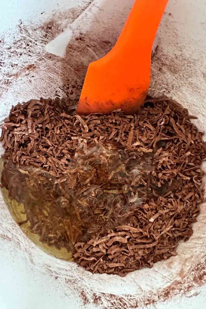 Chocolate and coconut in a bowl with an orange spatula.