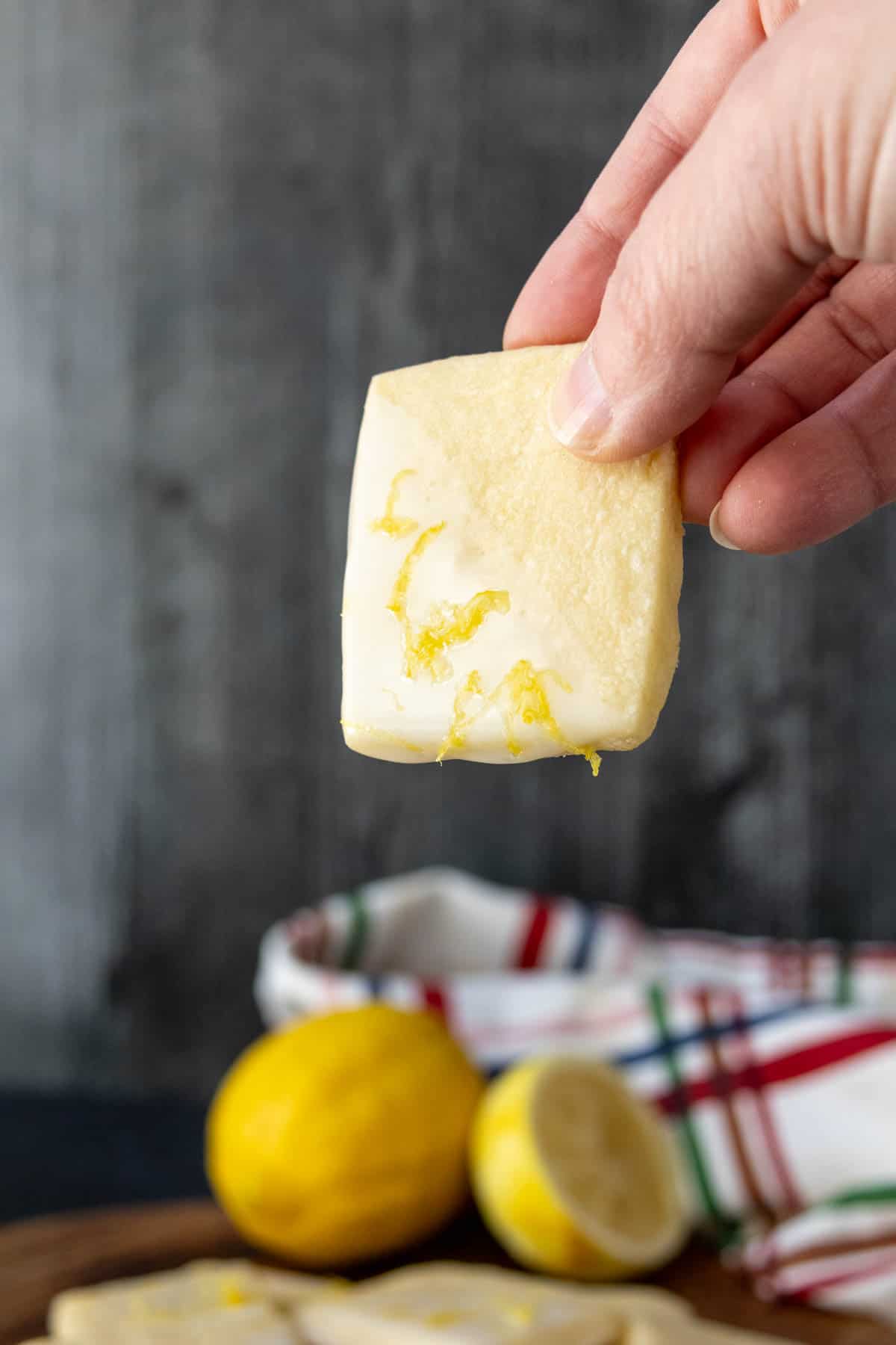 A hand holding a lemon cookie over a cutting board.