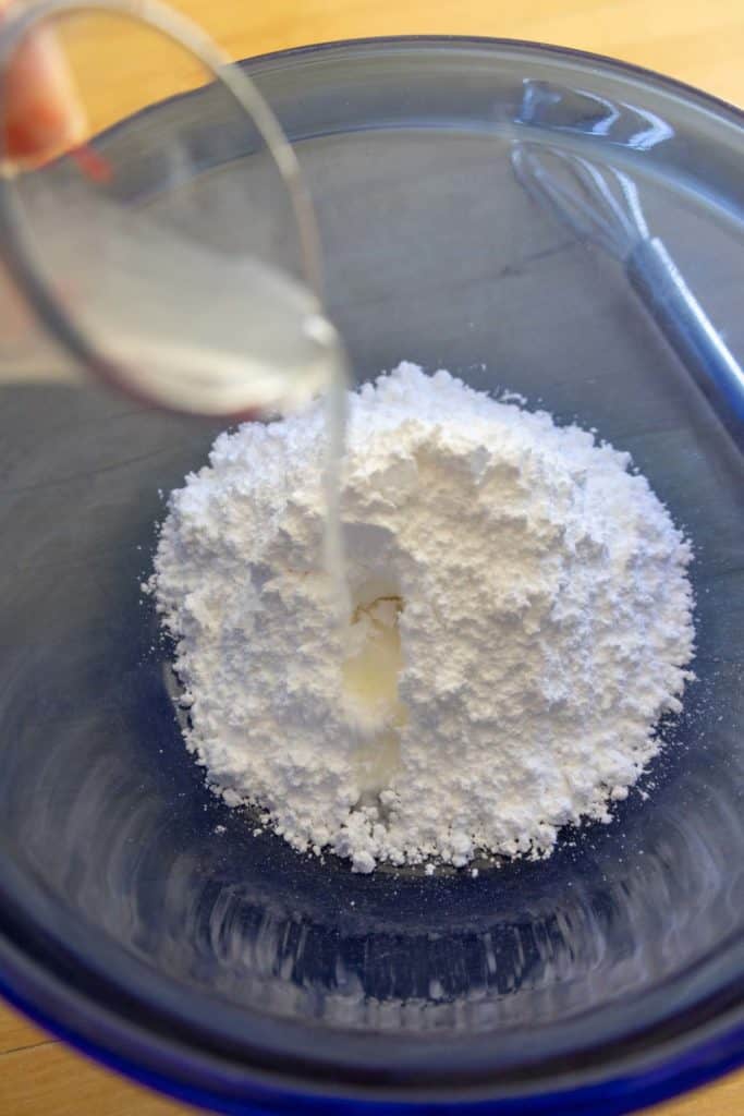 A person pouring lemon juice into powdered sugar in a bowl.