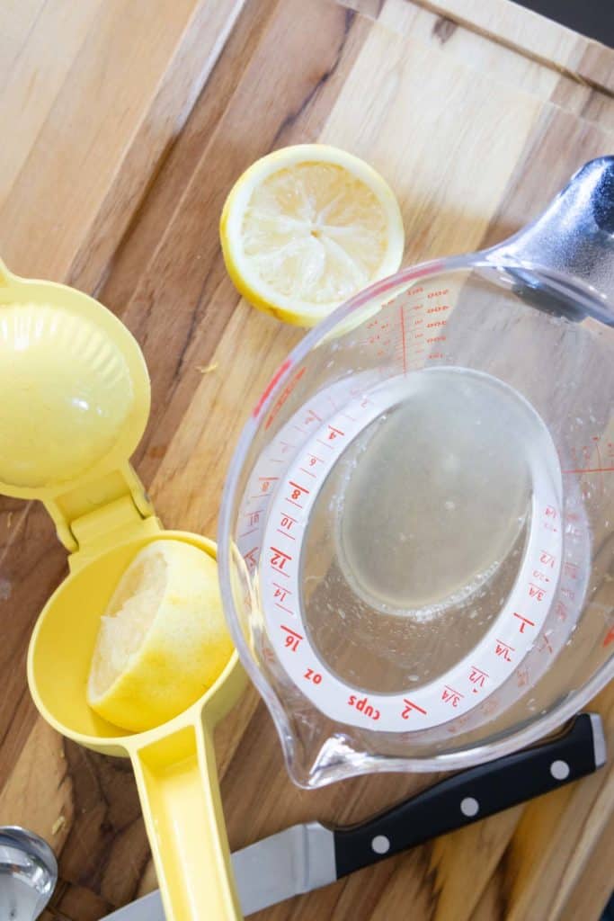 A measuring cup with lemons and measuring spoons on a cutting board.