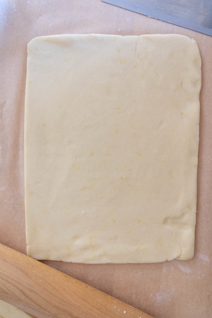 A square of dough on a baking sheet with a rolling pin.
