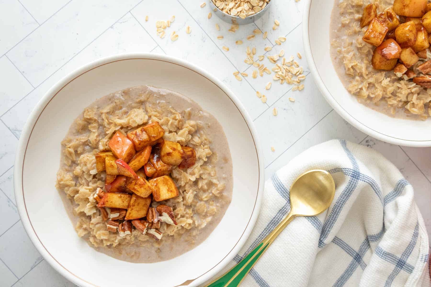 Two bowls of oatmeal with apples and oats on a table.