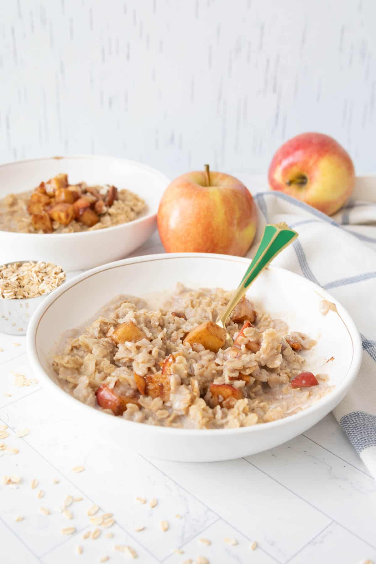Two bowls of oatmeal with apples and oats on a table.