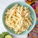 A bowl of jicama salad with limes and lime wedges.