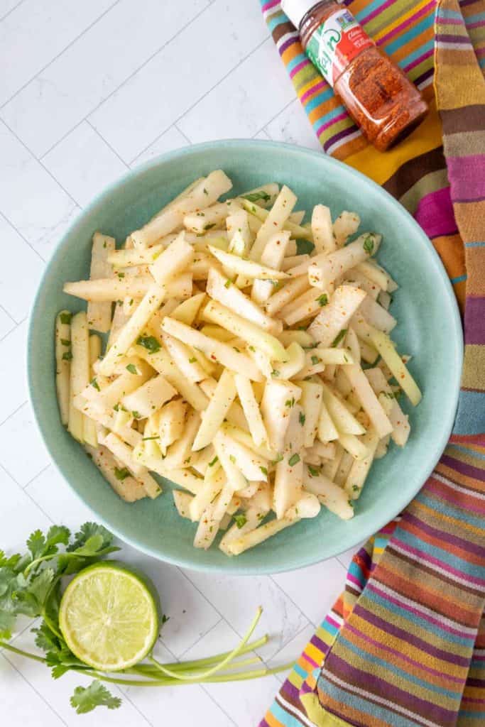 A bowl of jicama salad with limes and lime wedges.