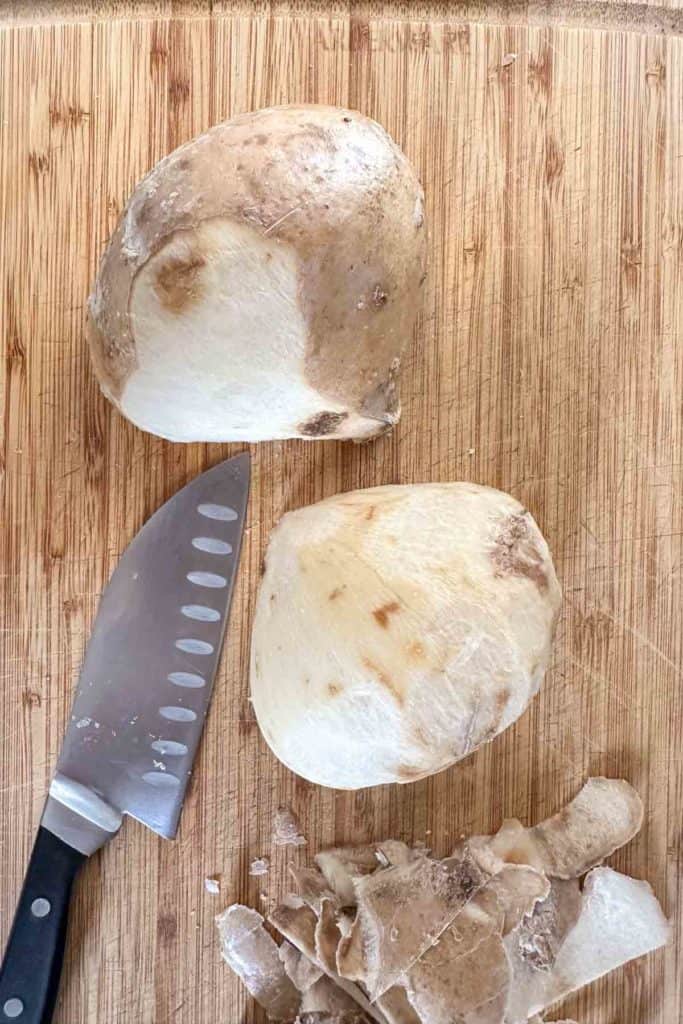 A knife on a cutting board next to two jicama halves.