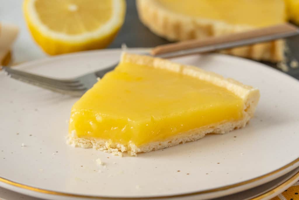 A slice of lemon tart on a plate with a fork.