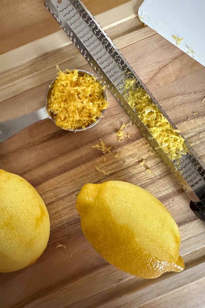 Two lemons on a cutting board next to a knife.