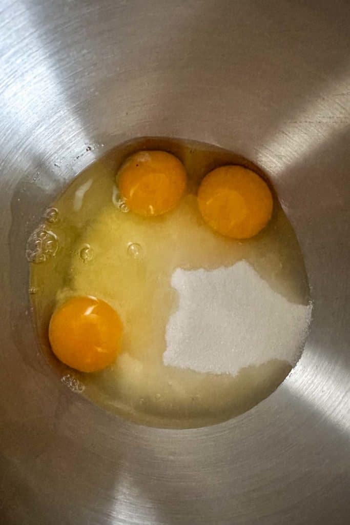Three eggs and sugar in a metal bowl.