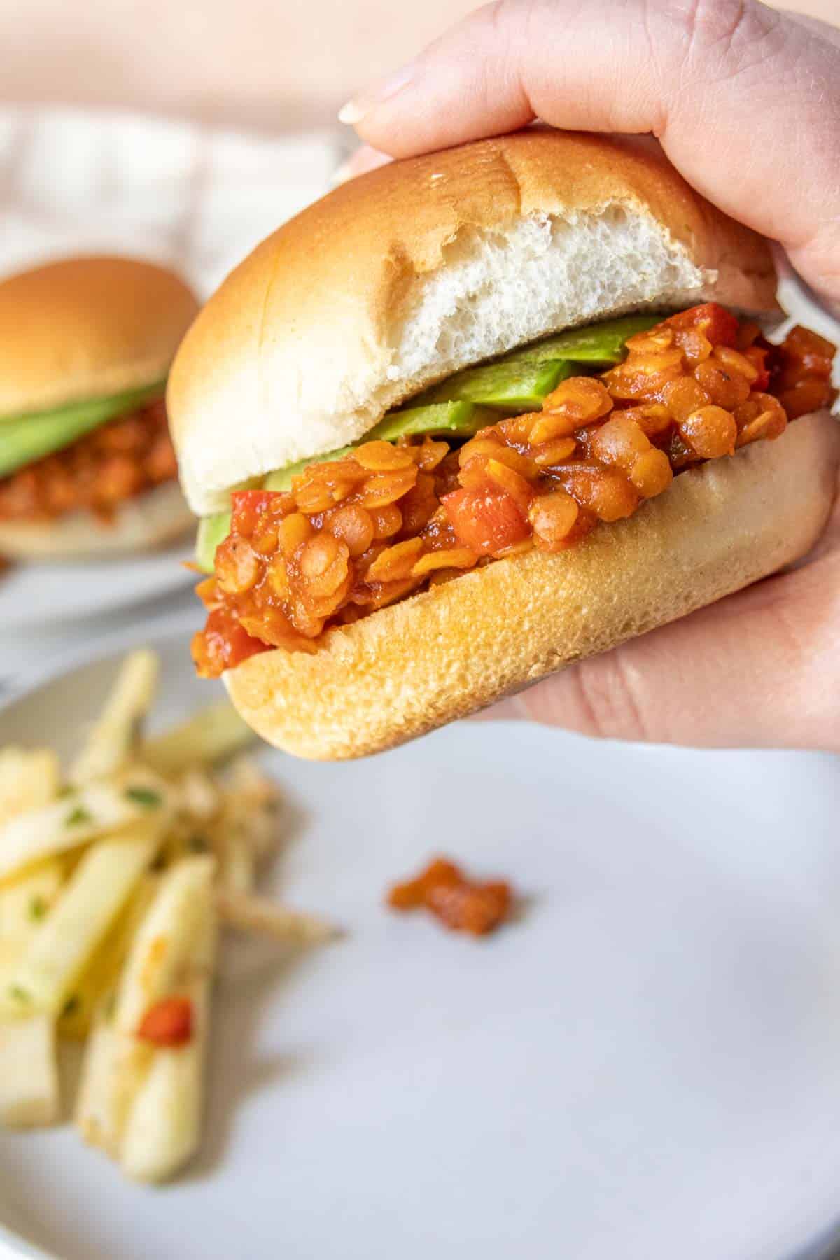 A person holding a sandwich with lentils and avocado.