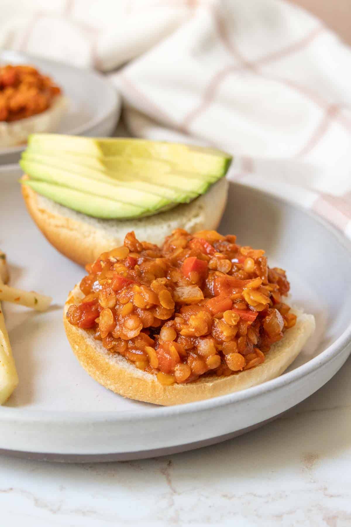 A plate with a sandwich with lentils and avocado on it.