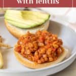 Open sandwich featuring vegan sloppy joes filling made from lentils on a bun, topped with sliced avocado on the top half, and served on a plate.