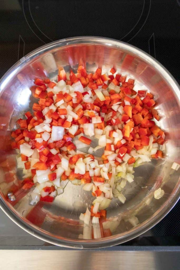 Sliced onions and peppers in a pan on top of a stove.