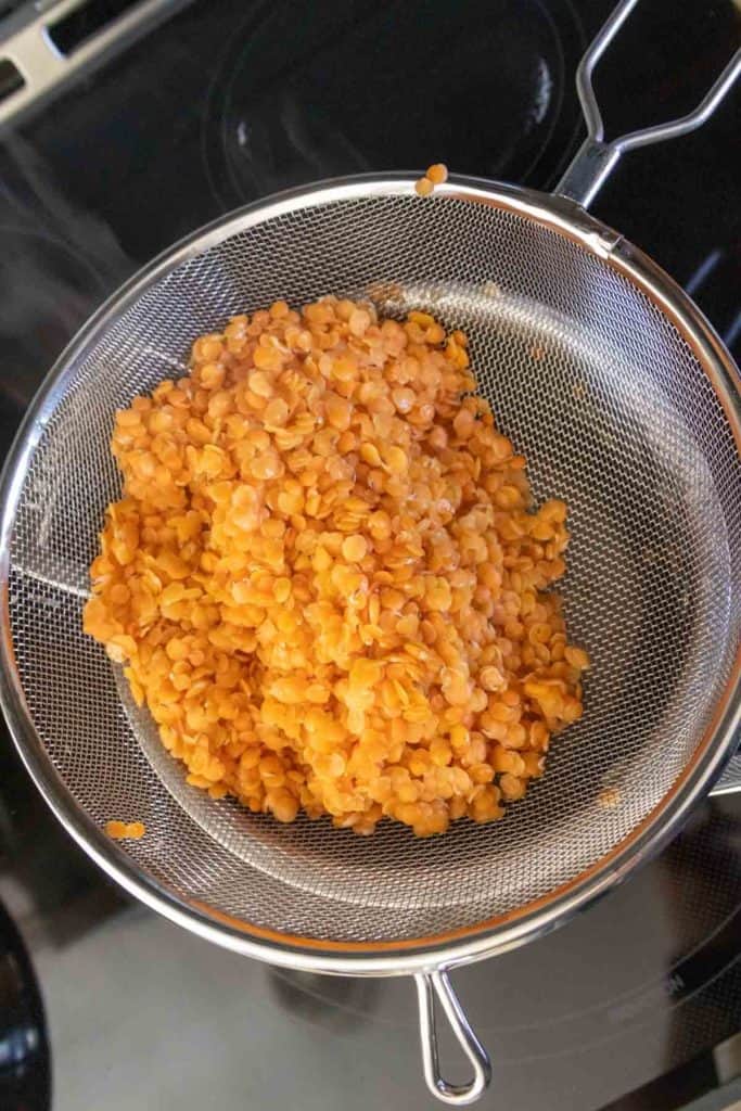 A metal strainer with lentils on top of a stove.