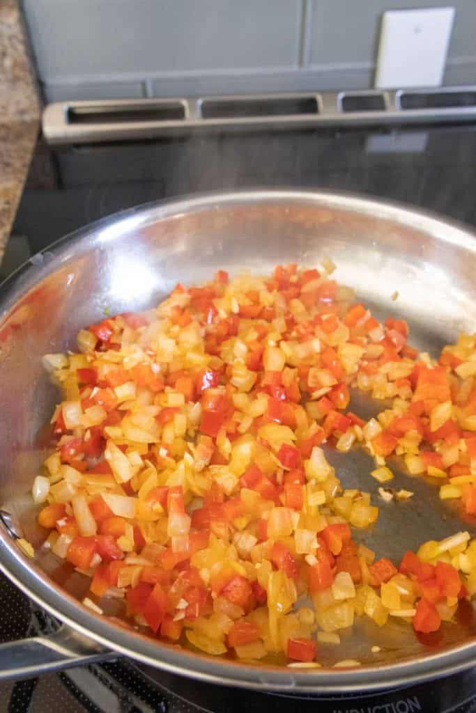 A frying pan with peppers and onions on the stove.