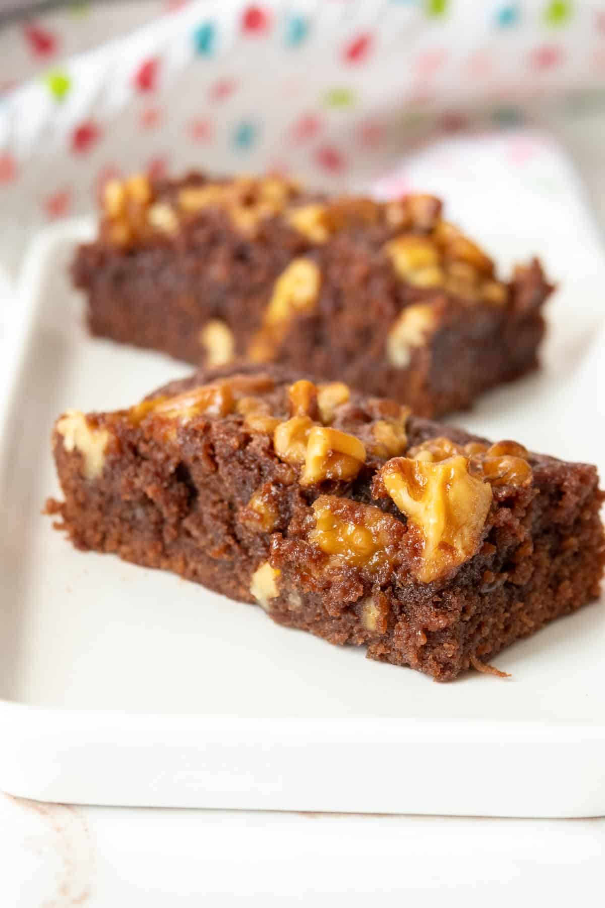 Two brownies with walnuts on a white plate.