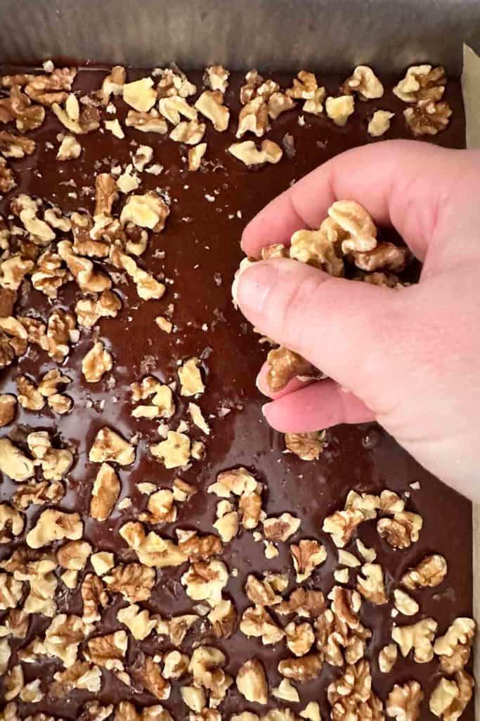 A hand is putting walnuts on a brownie batter.