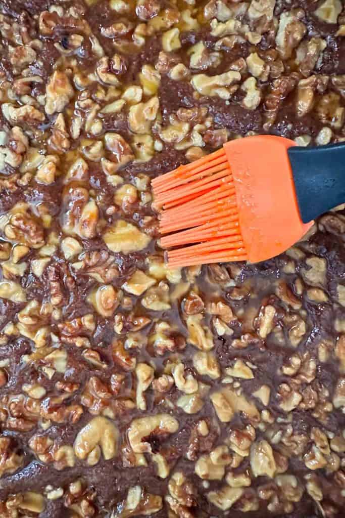 An orange spatula is being add glaze to brownies.