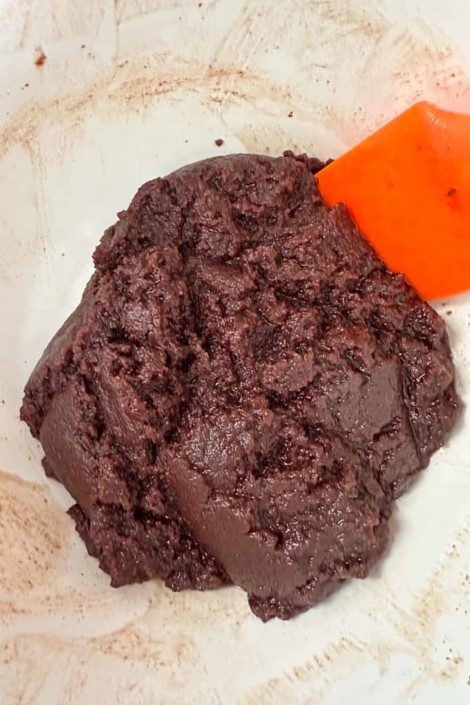 Chocolate brownie batter in a bowl with an orange spatula.