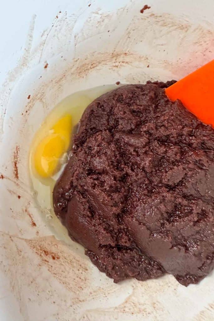 A bowl of chocolate batter with an egg in it.