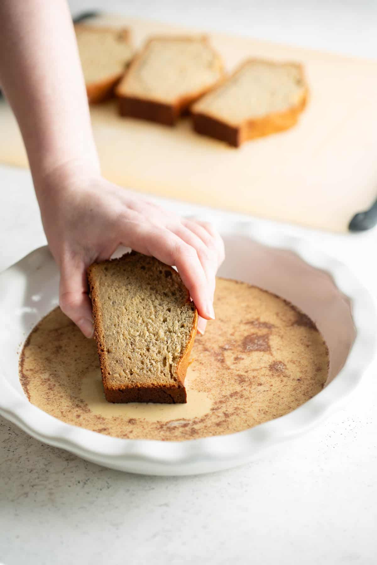 A person dipping banana bread into french toast custard.