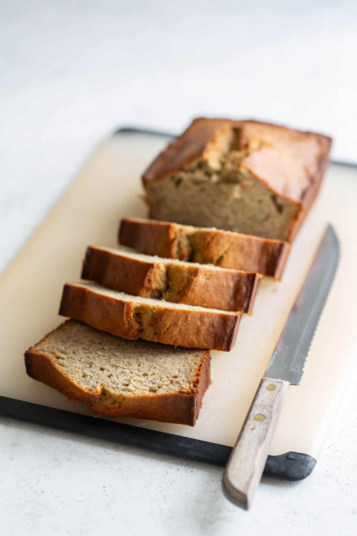 Sliced banana bread on a cutting board with a knife.