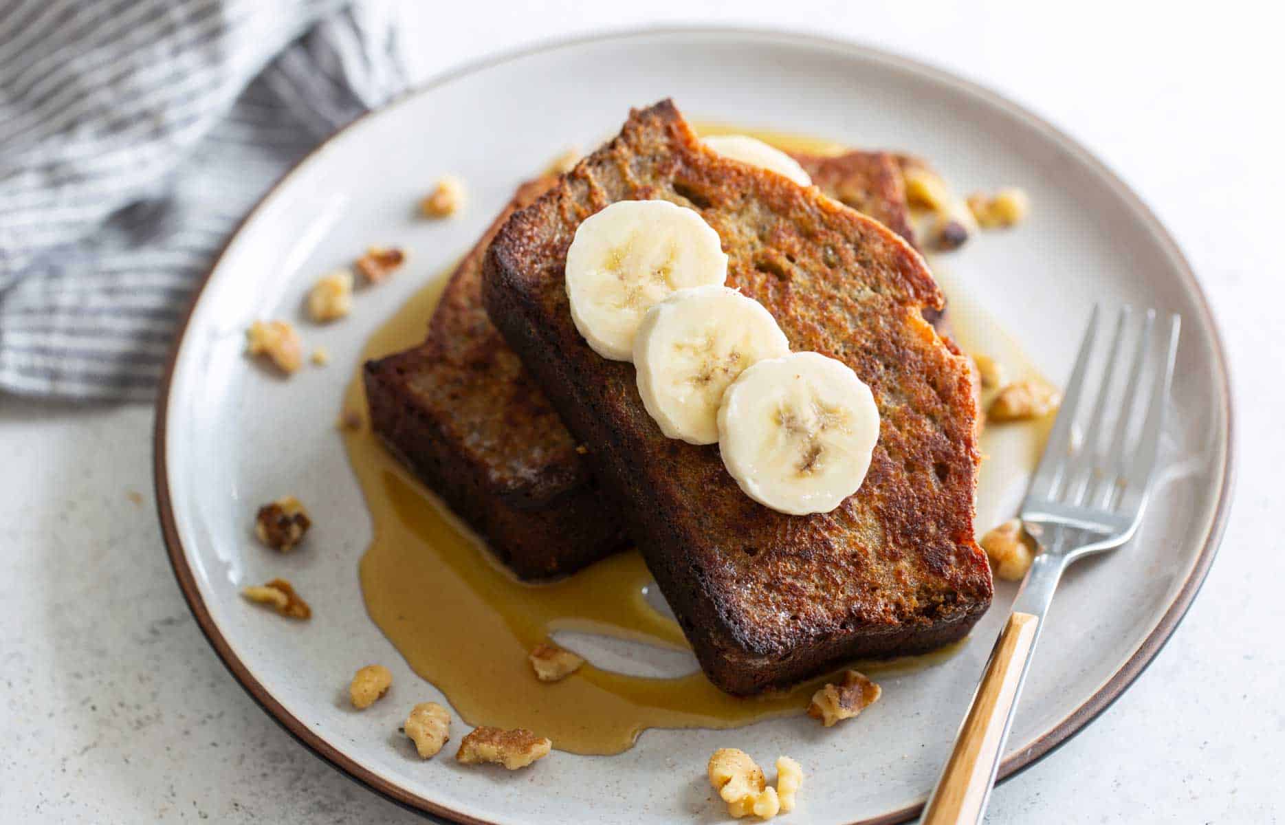 French toast with bananas and walnuts on a plate.