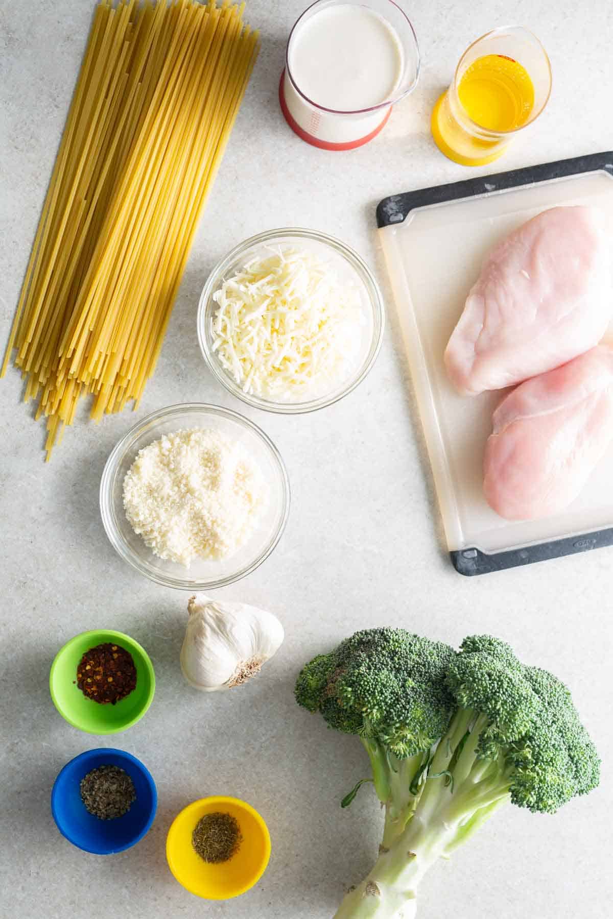 Ingredients for chicken and broccoli pasta on a white table.