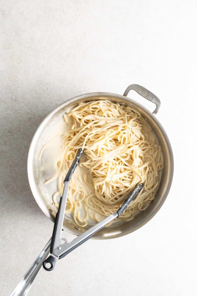 A pan with noodles in it and a pair of tongs.