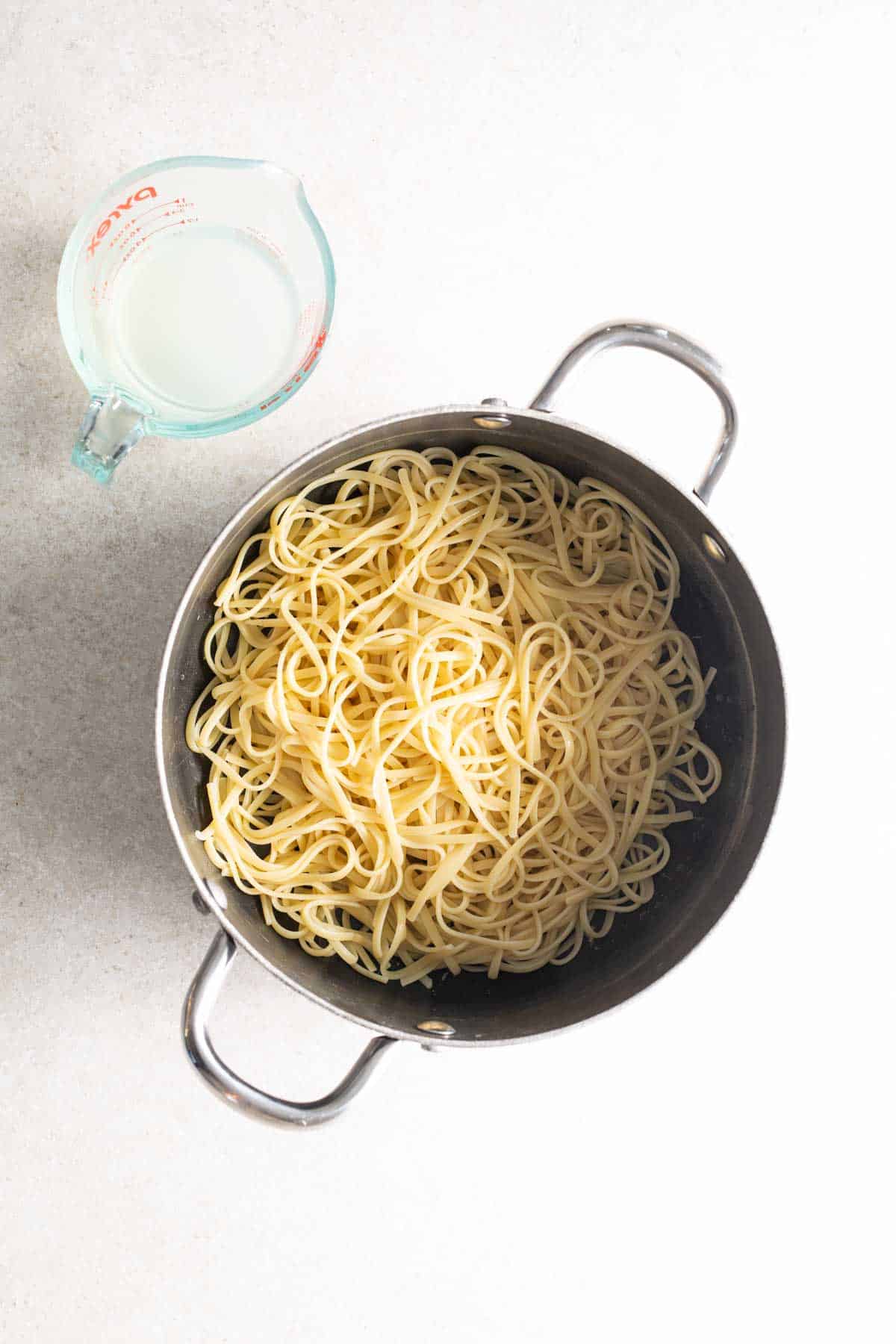 Pasta in a pan next to a measuring cup.