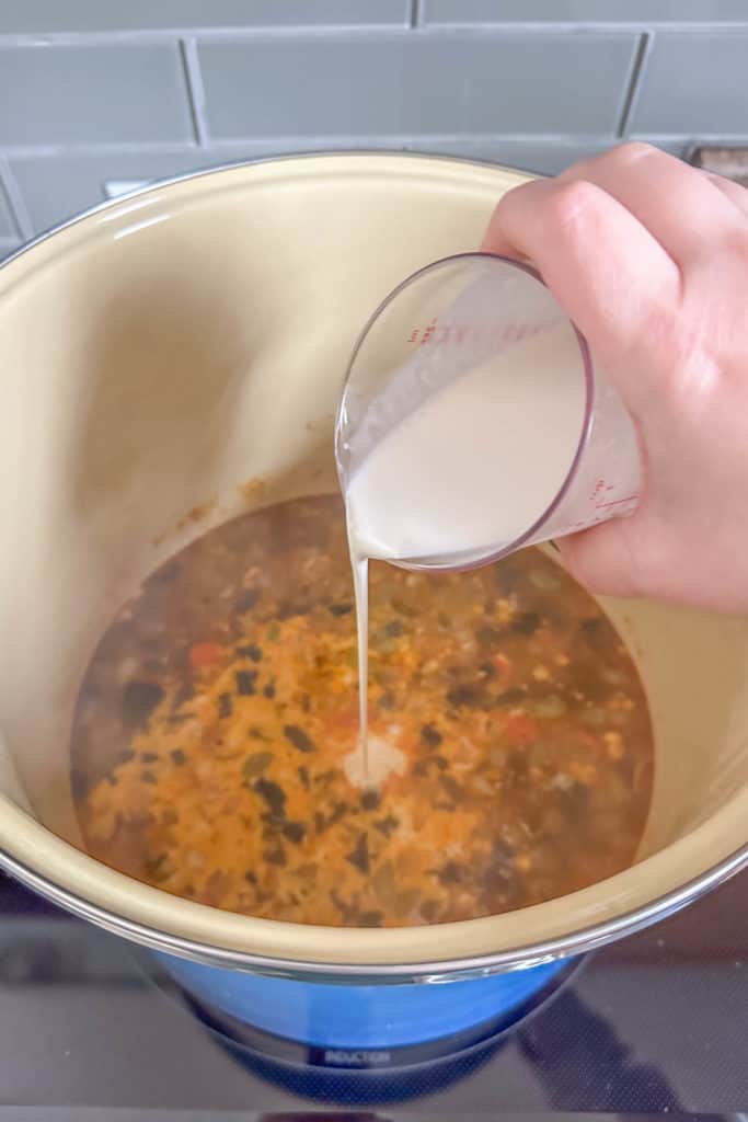 A person pouring milk into a bowl of soup.