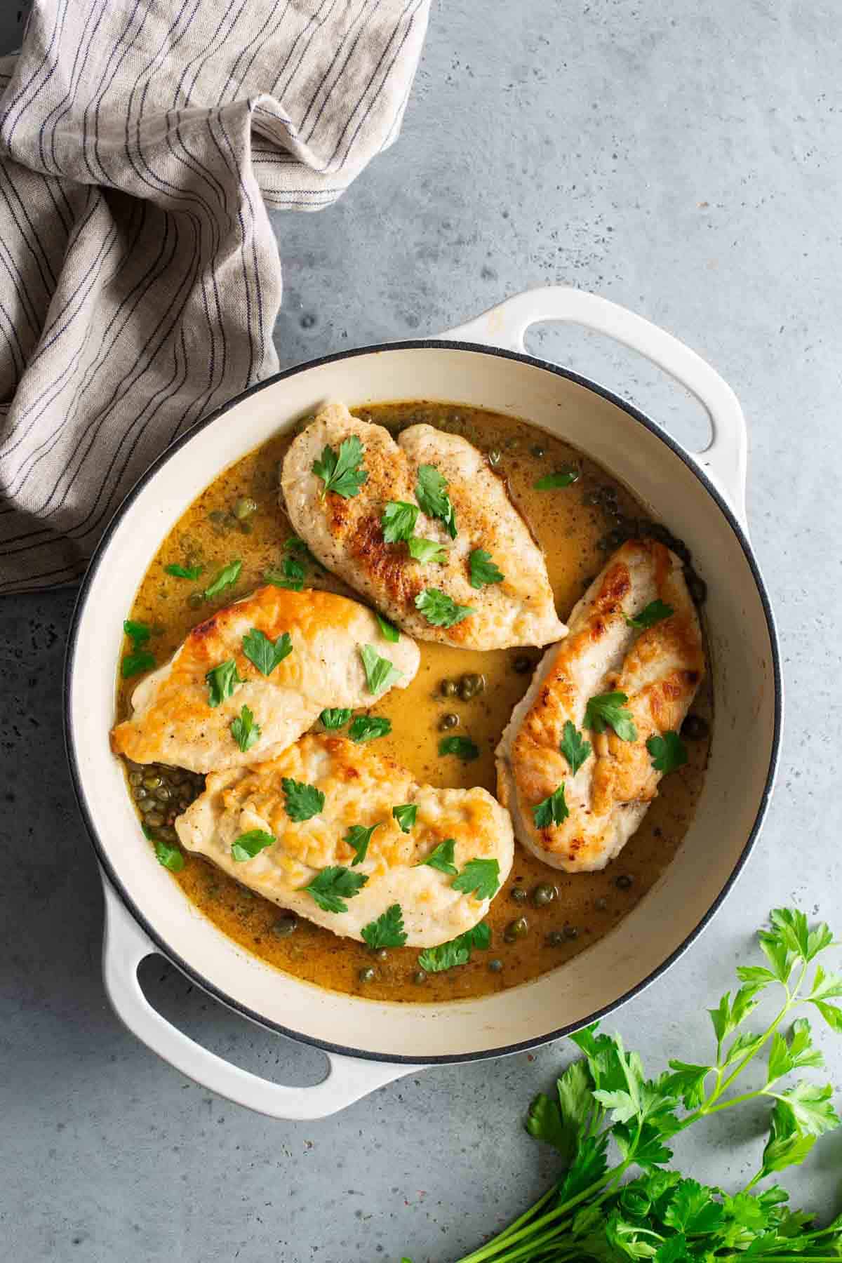 Chicken breasts in a sauce in a pan with parsley.