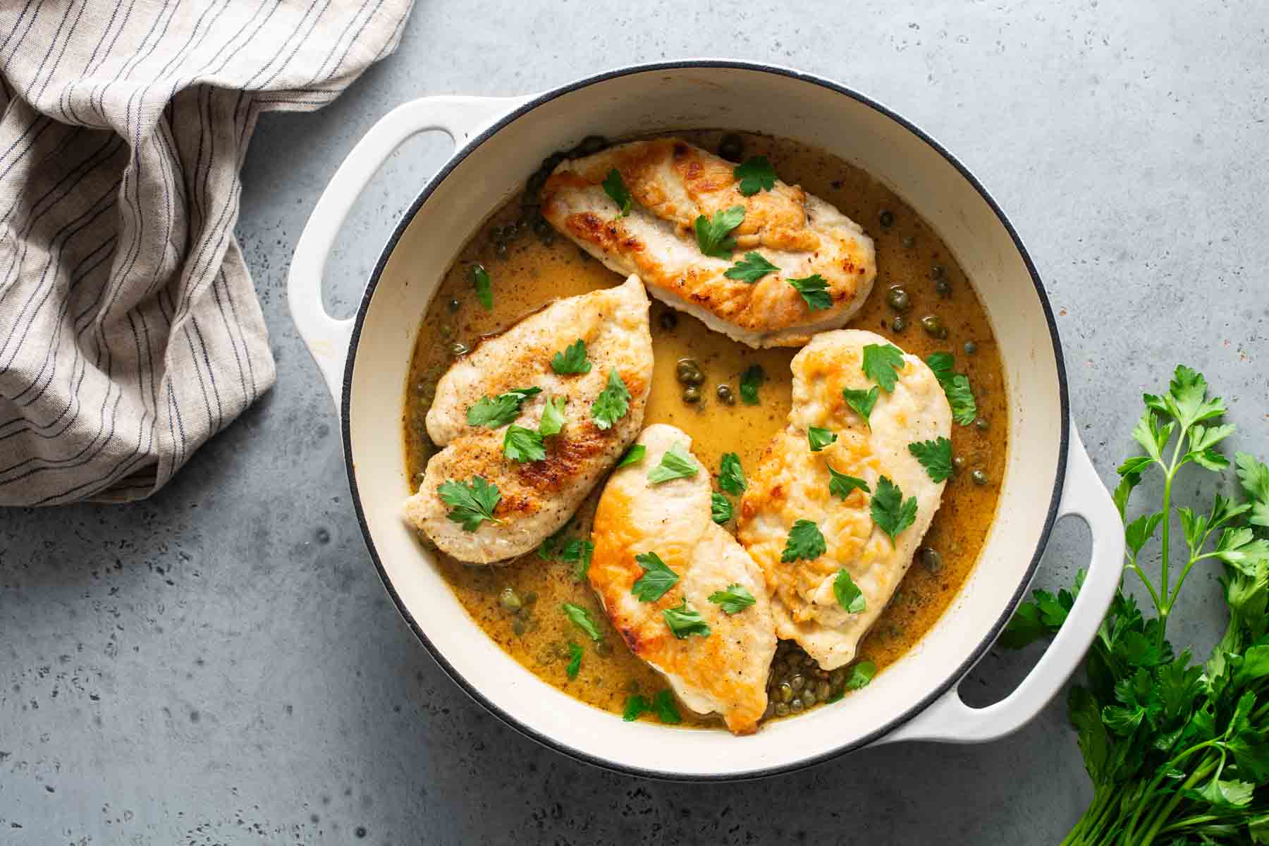 Chicken breasts in a sauce in a white pan with parsley.