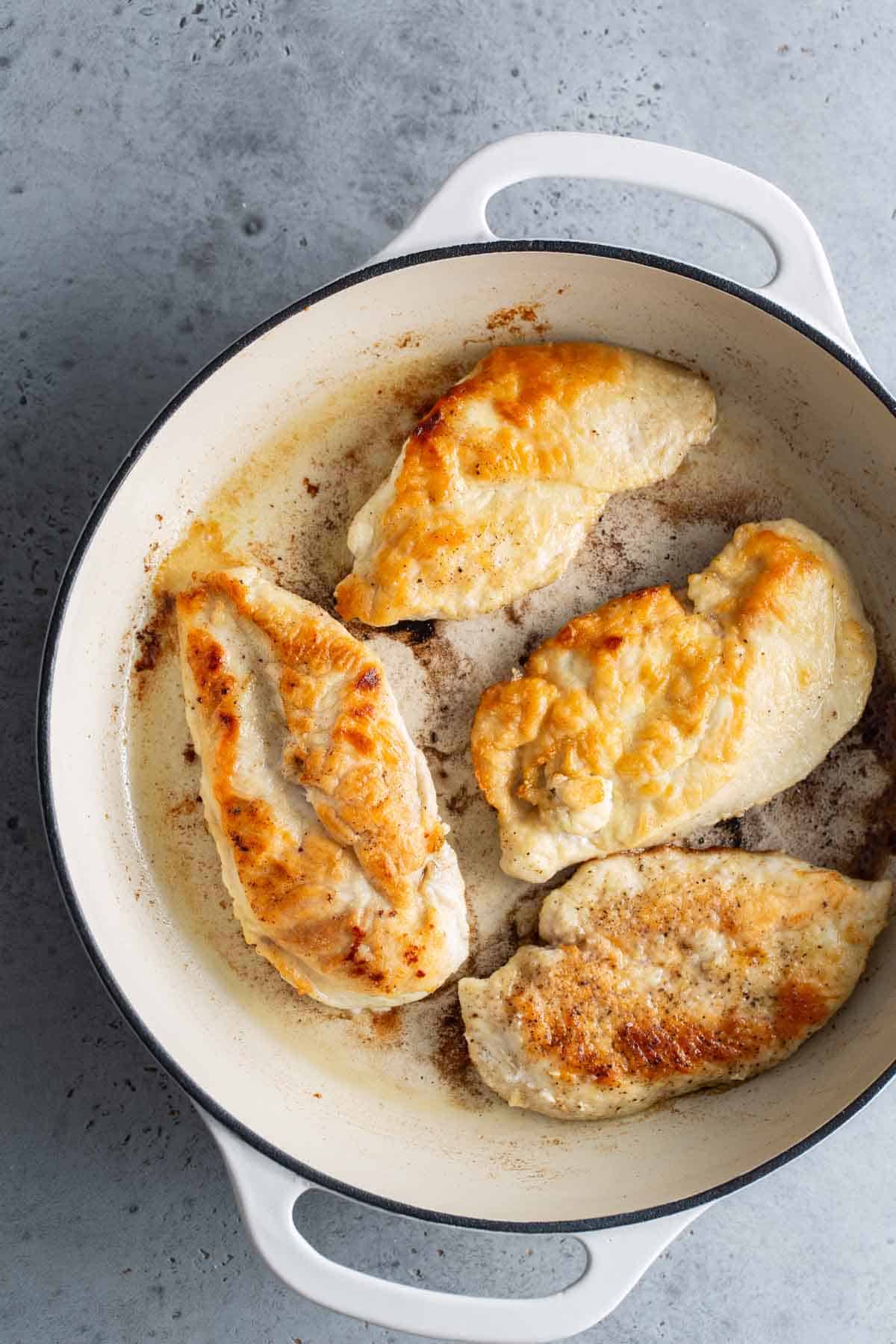 Chicken breasts in a skillet on a gray background.