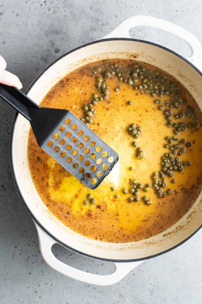 A person using a spatula to stir the capers in a pan.